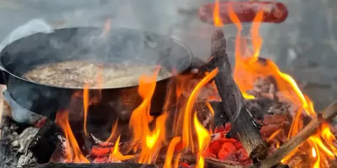 Matlagning över öppen eld, en härlig del av sportlov aktiviteter. Korv och mat i panna över flammande ved.