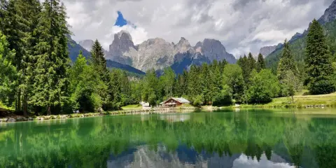 Riflessi perfetti sul lago Welsperg, con montagne maestose e una baita accogliente tra gli alberi.