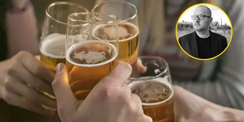 Ludzie wznoszą toasty piwem, podczas gdy w tle widać mężczyznę w okularach, który może symbolizować problem z alkoholem.