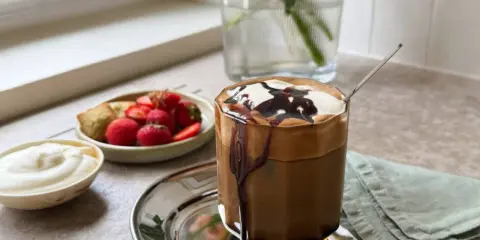 En läcker frappe med chokladsås och grädde, serverad med färska jordgubbar och en bit bakverk. Ett perfekt frappe recept för en solig dag.