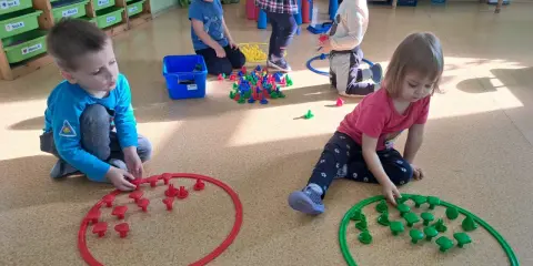 Dzieci w przedszkolu bawią się klockami, tworząc wzory w obręczach. To świetne zabawy dla 3 latka w przedszkolu.