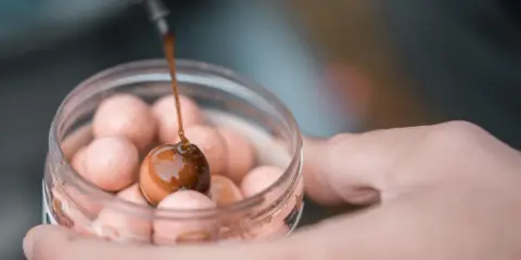 Karpie oszaleją na widok tego dobrego dipu na karpia! Ciemny płyn spływa na kulkę zanętową w słoiczku.
