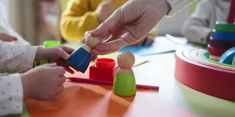 Dzieci bawią się drewnianymi ludzikami. W żłobku od jakiego wieku można zapisać dziecko?