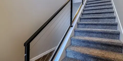 Miękka wykładzina na schody betonowe zapewnia komfort i bezpieczeństwo. Nowoczesna balustrada z linkami dodaje elegancji.