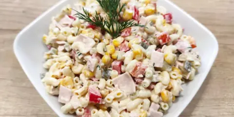 Pyszna sałatka z makaronem i szynką, kukurydzą, papryką i ogórkiem, udekorowana gałązką koperku.