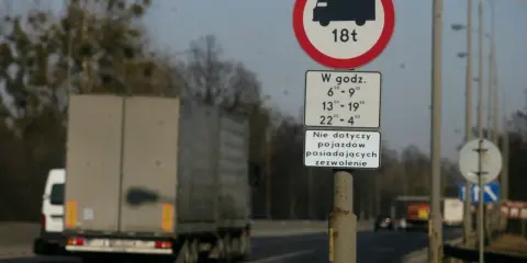 Znak zakazu ruchu dla ciężarówek powyżej 18t w określonych godzinach. Czy ciężarówki mogą jeździć w niedzielę? Ten znak odpowiada.
