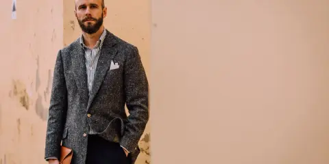 Man in a textured grey jacket and black pants, holding a tan envelope clutch.