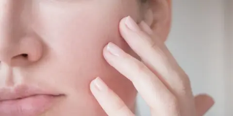 Dita accarezzano delicatamente il viso, mostrando una pelle reattiva e sensibile, bisognosa di cure delicate.