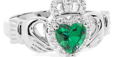 Anello Claddagh con cuore verde smeraldo, circondato da diamanti e sormontato da una corona scintillante.
