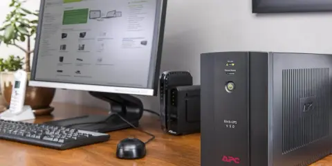 Un onduleur ordinateur APC protège votre équipement des coupures de courant. Il est placé sur un bureau en bois, à côté d'un écran d'ordinateur.