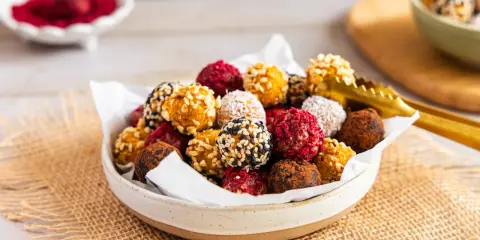 Schüssel voller bunter Energy Balls, perfekt für ein schnelles energy balls rezept. Mit Nüssen, Kokos, Kakao und Beeren verfeinert.