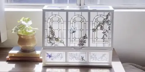 Boîte à bijoux ornée de vitraux décoratifs représentant des papillons et des fleurs, posée sur une commode en bois.