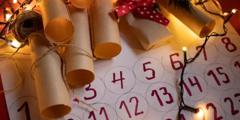 Un **calendario avvento fai da te cartoncino** con rotoli di carta marrone legati con spago, luci natalizie e un piccolo pacchetto regalo.