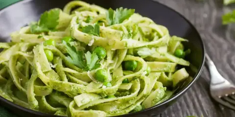 Pyszne tagliatelle z zielonym pesto, groszkiem i listkami pietruszki w czarnej misce.