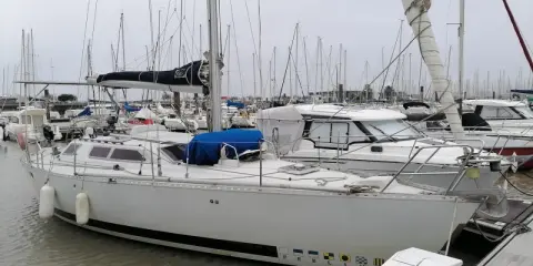 Un voilier blanc, "PEELIN", est amarré dans un chantier naval. D'autres bateaux sont visibles en arrière-plan.