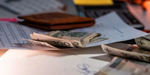 Pieniądze na dokumentach, portfel i klawiatura. Symbolizują wsparcie finansowe, np. refundację pieluchomajtek dla osób ze znacznym stopniem niepełnosprawności.