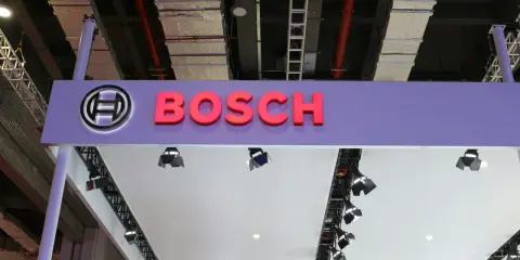 Logo Bosch i nazwa firmy na fioletowym tle. W tle widać instalacje przemysłowe, przewody i drabiny, sugerujące miejsce, gdzie odbywa się produkcja.