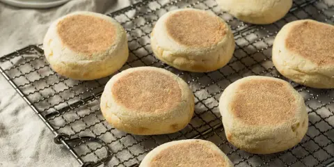 Plusieurs muffins anglais dorés et moelleux refroidissent sur une grille. Parfaits pour le petit-déjeuner.