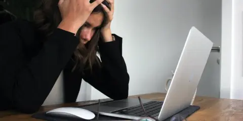 Kobieta z rękami na głowie przy laptopie, symbolizująca wypalenie i decyzję o porzuceniu pracy.
