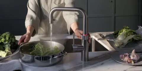 Person kocht Brokkoli mit heißem Wasser aus einem Quooker. Manche fragen sich, ob ein Quooker ungesund ist, aber hier wird er für gesunde Ernährung genutzt.