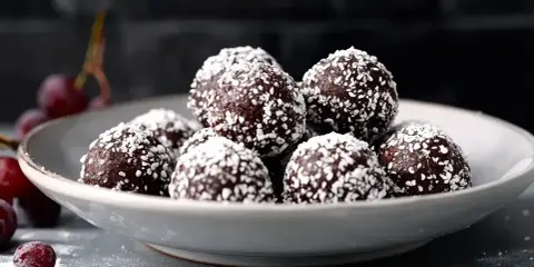 En skål med chokladbollar, perfekta för ett enkelt chokladbollar recept. Garnerade med kokosflingor och med några körsbär bredvid.