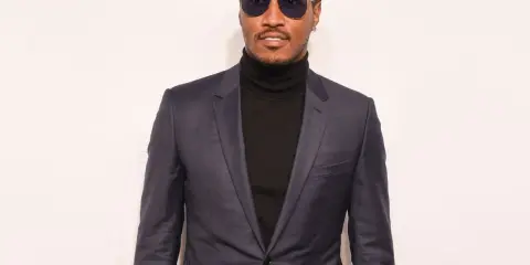 A man in a sharp black suit with a turtleneck, sporting stylish sunglasses.