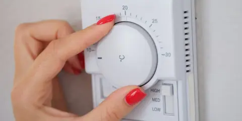 Mano ajustando el termostato para el cálculo de calefacción de la vivienda. La temperatura se muestra en grados Celsius.