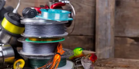 Stos szpul z żyłką i plecionką na spinning, obok kolorowe przynęty. Wybór między żyłką czy plecionką na spinning zależy od łowiska.