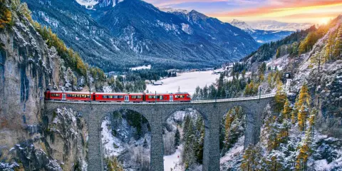 Roter Zug überquert eine Steinbrücke in verschneiter Schweizer Alpenlandschaft. Ein perfektes reiseziel schweiz.
