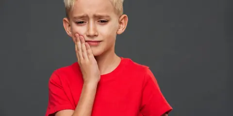 Un jeune garçon blond, le visage crispé, se tient la joue. Il semble triste, comme si mon fils se sent mal aimé.