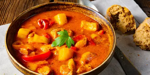 Aksamitna zupa gulaszowa, przepis babci, z kawałkami mięsa, ziemniaków i papryki, udekorowana natką pietruszki.