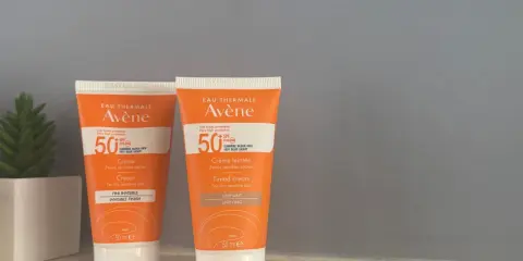 Deux tubes de spray solaire invisible SPF 50 Avène, l'un teinté, l'autre non, pour une protection optimale.