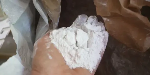 Main d'une personne tenant une poudre blanche fine, de la chaux morte, sortant d'un sac en papier.