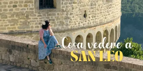 Donna seduta su un muretto di pietra, con vista panoramica. Un'ottima pausa durante il trekking a San Leo.