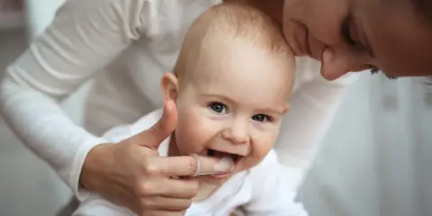 Mama pomaga dziecku z kolejnością wychodzenia zębów, delikatnie masując dziąsła palcem w nakładce.