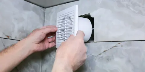 Installation d'une grille de ventilation VMC pour lutter contre la condensation dans une salle de bain carrelée.