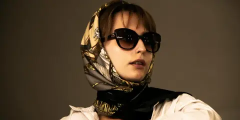 Donna con occhiali da sole e un elegante outfit con foulard annodato al collo, che incornicia il viso.
