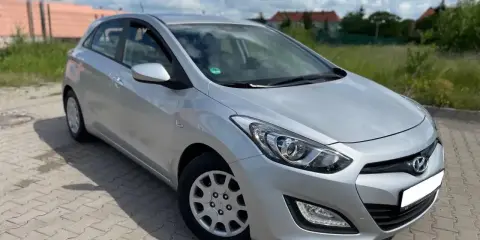 Srebrny Hyundai i30 1.4 benzyna zaparkowany na kostce brukowej, w tle zielona trawa i budynki.