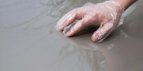 Dłoń w rękawiczce ochronnej dotyka lśniącego, szarego lakieru samochodowego.