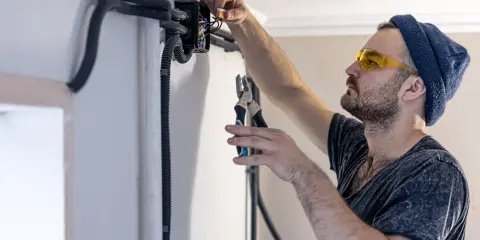 Elektryk w okularach ochronnych montuje przewody bezhalogenowe w puszce instalacyjnej, używając szczypiec.