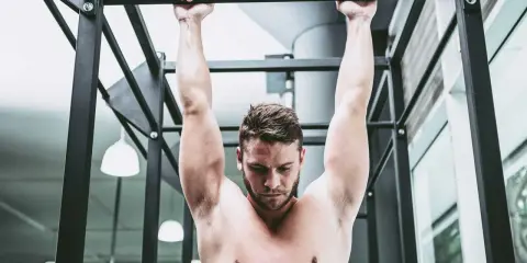 Uomo a torso nudo esegue trazioni alla sbarra, concentrato sul movimento per rafforzare la muscolatura.