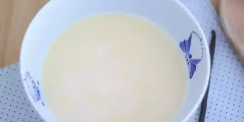 En skål med krämig vaniljsås, perfekt för ditt vaniljsås recept. En vaniljstång ligger bredvid.