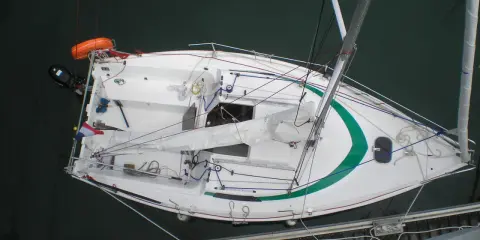 Voilier blanc avec une bande verte, prêt pour une sortie tonique. 23 avis positifs sur sa performance.