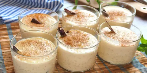 Seis copas de cremoso arroz con leche, espolvoreado con canela y decorado con una rama de canela.
