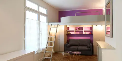 Aménagement petit studio optimisé avec lit mezzanine, canapé confortable et rangements intégrés. Un espace de vie fonctionnel et stylé.