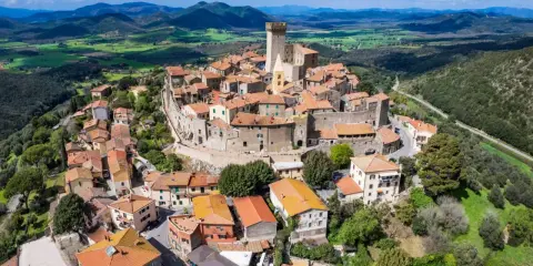 Un borgo medievale con un castello domina le colline toscane. Perfetto per un weekend in Toscana, tra tetti rossi e panorami mozzafiato.