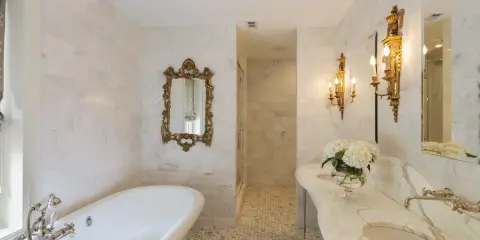 Elegancka łazienka w stylu francuskim z wolnostojącą wanną, marmurowymi blatami i złotymi zdobieniami.