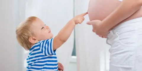Mały chłopiec w pasiastej koszulce dotyka paluszkiem brzucha mamy, która jest w 25 tygodniu ciąży.