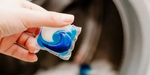 Mano sostiene una cápsula de detergente azul y blanca lista para usar en la lavadora.