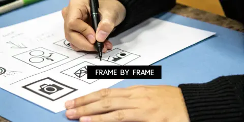 Mano dibujando bocetos de iconos en papel, como una cámara y un sobre. El texto "FRAME BY FRAME" aparece en un recuadro negro.